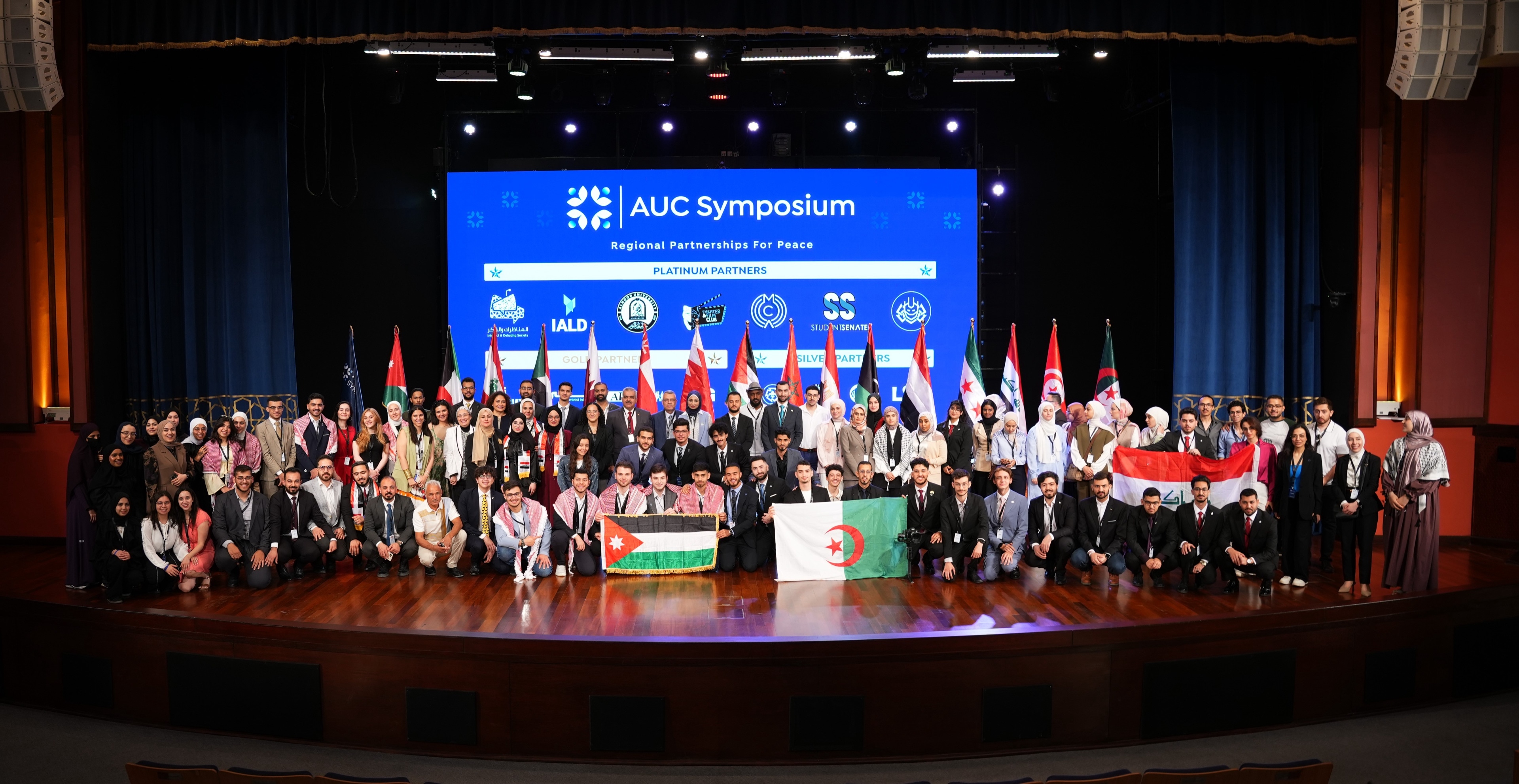 Participants of the AUC Symposium gathered on stage with the flags of the region